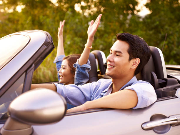 young couple enjoying a car ride young asian couple riding in a convertible sport car at sunset. happy malay couple stock pictures, royalty-free photos & images