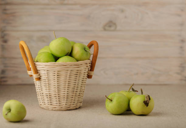 Green apples in a wicker basket on a wooden light background. Selectuve focus.