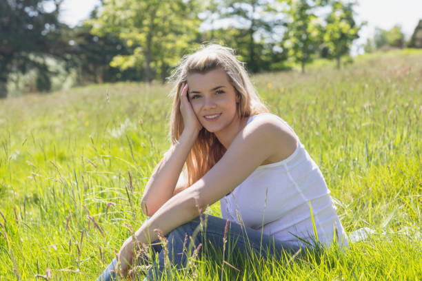 istock Pretty blonde smiling at camera sitting on grass 817338604