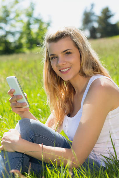 istock Pretty blonde sitting on grass sending a text 817338734