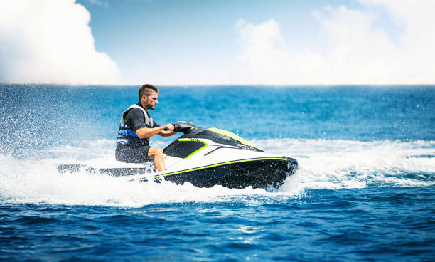 Jet skiing. Closeup side view of a young man riding a jet ski on a sunny summer day at open sea. He's wearing swimming suit and a life jacket. neoprene photos stock pictures, royalty-free photos & images