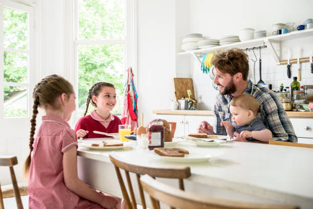 istock Father sitting at breakfast table with two daughters and baby son 817347982