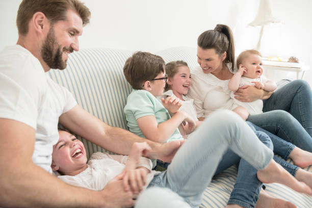 Father tickling daughter on sofa, mother talking to three young children Family at home with four children having fun together, laughing and smiling 6 11 months stock pictures, royalty-free photos & images