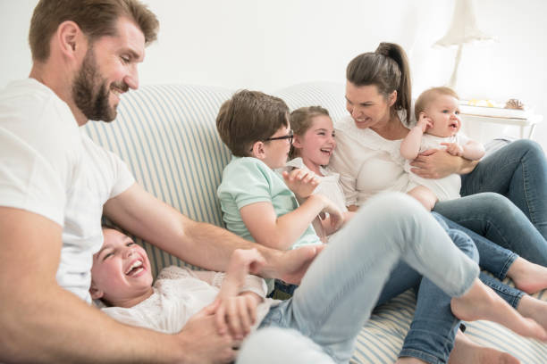 Father tickling daughter on sofa, mother talking to three young children Family at home with four children having fun together, laughing and smiling london girl stock pictures, royalty-free photos & images