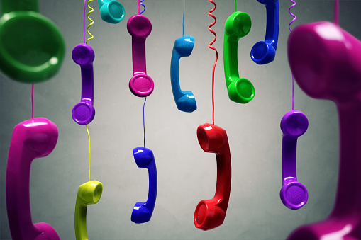 Red and multi-coloured telephone receiver hanging over gray background concept for on the phone, customer service, on hold or contact us