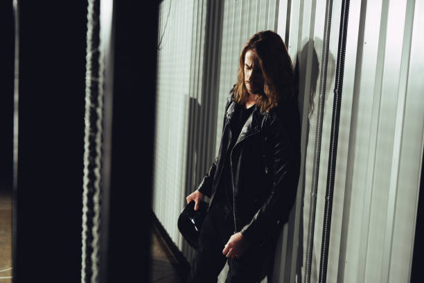 istock Pensive young long haired man holding helmet and leaning at wall 817348906