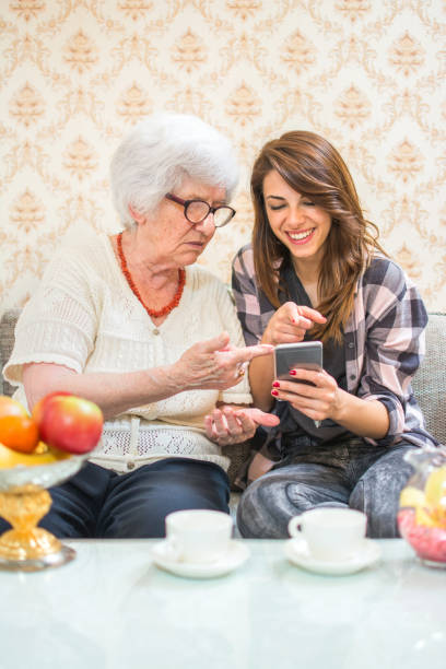 grand-mère et sa petite-fille, commentant les médias sociaux se nourrit de téléphone intelligent. - women telephone senior adult on the phone photos et images de collection