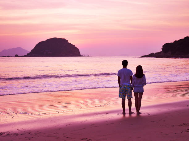 young asian couple walking on beach during sunrise young asian couple taking a walk on beautiful beach before sunrise. malay couple full body stock pictures, royalty-free photos & images