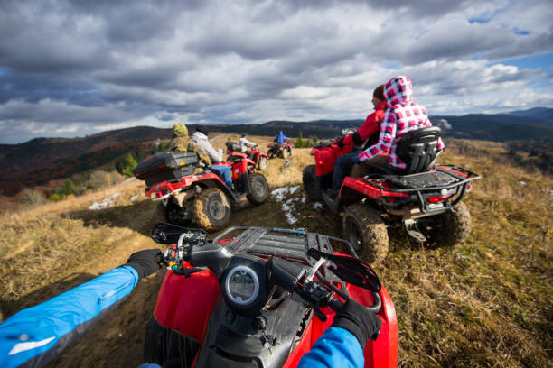 découvre de l’atv, un groupe de personnes à un vélo quad sur une route de montagne, sous un ciel avec nuages en automne - off road vehicle quadbike quad racing motocross photos et images de collection