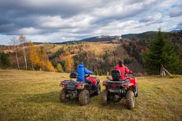 vista traseira de dois homens sentados em quad bikes, apreciando a bela paisagem de montanhas e florestas coloridas sob o céu com nuvens cumulus no outono - off road - fotografias e filmes do acervo
