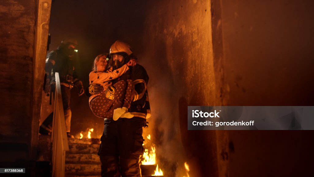Brave Fireman Descends Stairs of a Burning Building with a Saved Girl in His Arms. Firefighter Stock Photo