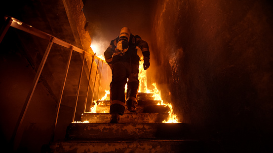 Fuerte y valiente bombero va hasta las escaleras en el edificio ardiente. Escaleras quema con llamas. photo