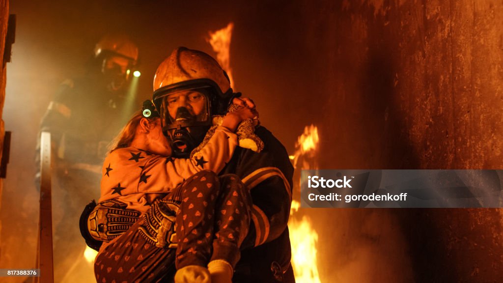 Valiente bombero desciende escaleras de un edificio ardiendo y tiene guardado la niña en sus brazos. Chimenea y un bombero en el fondo. - Foto de stock de Bombero libre de derechos