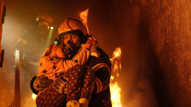勇敢な消防士は燃えているビルと彼の腕の中で女の子を保存を保持の階段を下る。暖炉とバック グラウンドで 1 つの消防士。 - salvation ストックフォトと画像