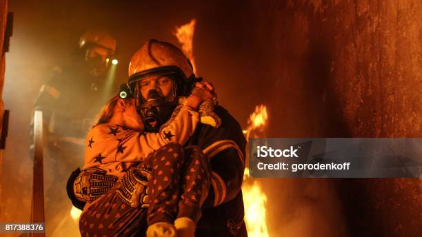 Brave Fireman Descends Stairs Of A Burning Building And Holds Saved Girl In His Arms Open Fire And One Firefighter In The Background Stock Photo - Download Image Now