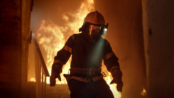istock Brave Firefighter With Switched On Flashlight on His Helmet Runs Down the Burning Stairs. Fire is Raging. 817388414