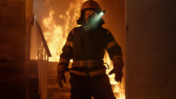 istock Brave Firefighter With Switched On Flashlight on His Helmet Standin Alone in Burning Staircase. Open Fire in the Background. 817388428