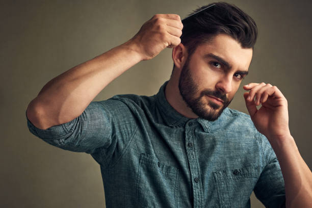 Beard season is here Studio shot of a handsome young man combing his hair against a grey background combing stock pictures, royalty-free photos & images