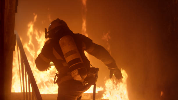 dzielny strażak biegnie po schodach. szalejący ogień jest widoczny wszędzie. - pożar zdjęcia i obrazy z banku zdjęć
