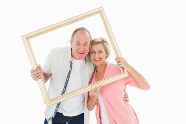 istock Older couple smiling at camera through picture frame 817405136