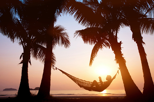 woman relaxing in hammock on beautiful sunset beach, holiday concept