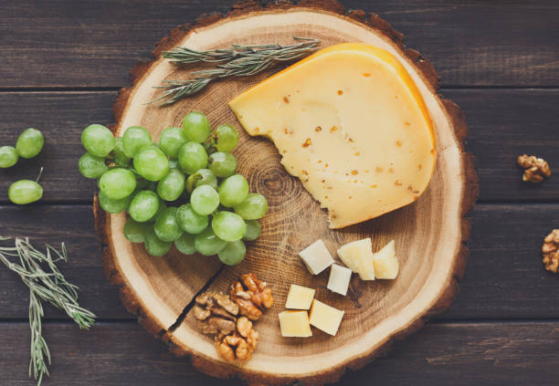 Cheese platter, gouda herb on natural wood disc with grapes and Cheese platter, gouda herb on natural wood disc with grapes and nuts, still life, top view gouda cheese stock pictures, royalty-free photos & images