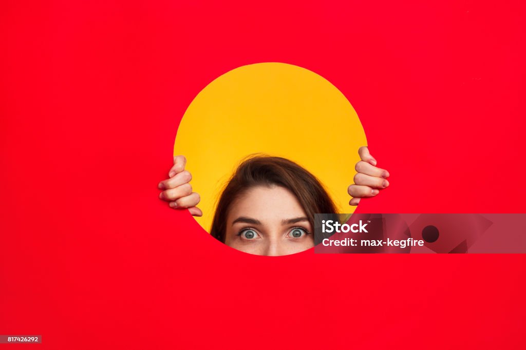 Woman in circle posing Crop woman looking out of circle cut in red paper on yellow background. Circle Stock Photo