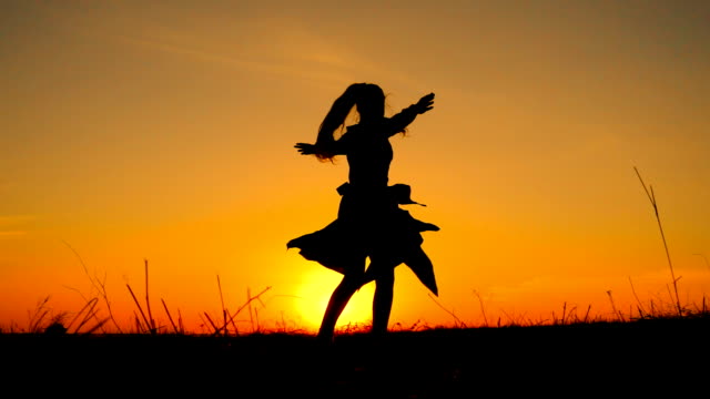 Silhouette of young witch dancing at field