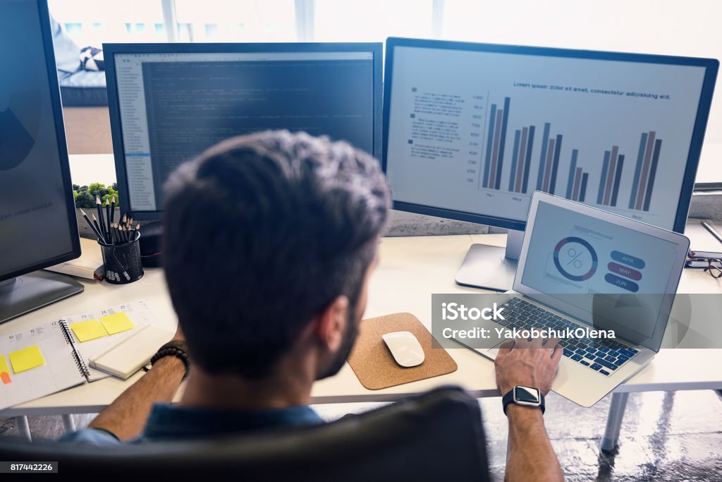 Male doing estimation on screen Man creating statistics in modern office. He working on digital devices while sitting at table and turning back to camera Analyzing Stock Photo