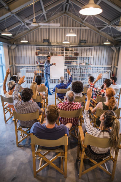 Rear view of large group of freelancers raising their arms during business seminar in a board room.