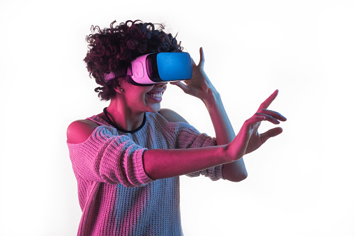 Young African woman smiling and touching air while having VR experience and adjusting goggles isolated on white.