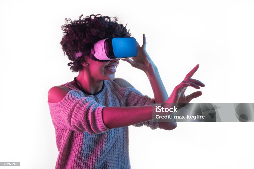 Woman adjusting VR headset and touching air Young African woman smiling and touching air while having VR experience and adjusting goggles isolated on white. Virtual Reality Simulator Stock Photo