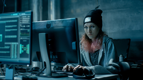 Nonconformist Teenage Hacker Girl Attacks and Hacks Corporate Servers with Virus. Room is Dark, Neon and Has Many Displays and Cables.