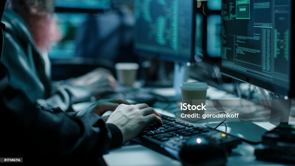 Close-up Shot of Hacker using Keyboard. There is Coffee Cups and Computer Monitors with Various Information. Vulnerability Stock Photo