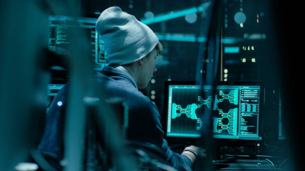 istock Back View of Teenage Hacker Working in Computer and Infecting with Virus Data Servers of Government Infrastructures. His Hideout is Dark with Many Monitors Around. 817486118