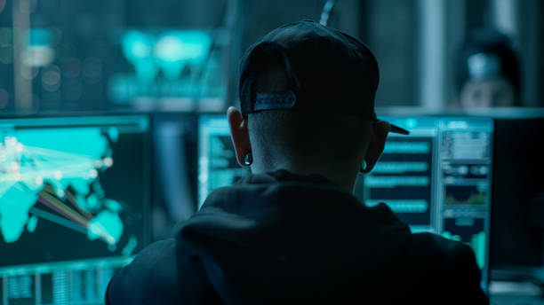 istock Close-up Frame from the Back of Working Hacker Organizing Advanced Virus Attack on Corporate Servers. Place is Dark and Has Multiple displays. 817486146