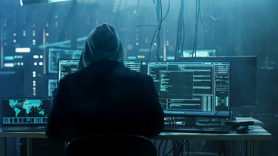 Peligroso Hacker encapuchado irrumpe en los servidores de datos gobierno e infecta su sistema con un Virus. Su lugar de escondite tiene atmósfera oscura, varias pantallas, Cables por todas partes. photo