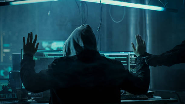 istock Fully Armed Special Cybersecurity Forces Soldier Arrests and Handcuffs Highly Dangerous Hacker. Hideout is Dark and Full of Computer Equipment. 817486268