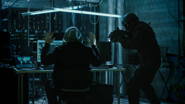 istock Fully Armed Special Cybersecurity Forces Soldier Arrests Highly Dangerous Hooded Hacker. Hideout is Dark and Full of Computer Equipment. 817486270