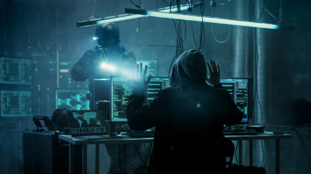 istock Fully Armed Special Cybersecurity Forces Soldier Arrests Highly Dangerous Hooded Hacker. Hideout is Dark and Full of Computer Equipment. 817486272