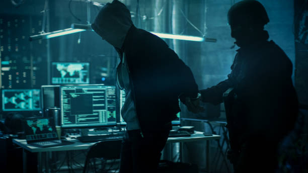 istock Fully Armed Special Cybersecurity Forces Soldier Arrests  and Handcuffs Highly Dangerous Hacker. Hideout is Dark and Full of Computer Equipment. 817486284