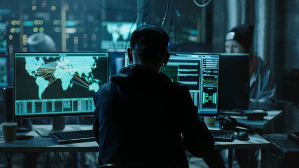istock Back View of Teenage Hacker Working in Computer and Infecting with Virus Data Servers of Government Infrastructures. His Hideout is Dark with Many Monitors Around. 817486362