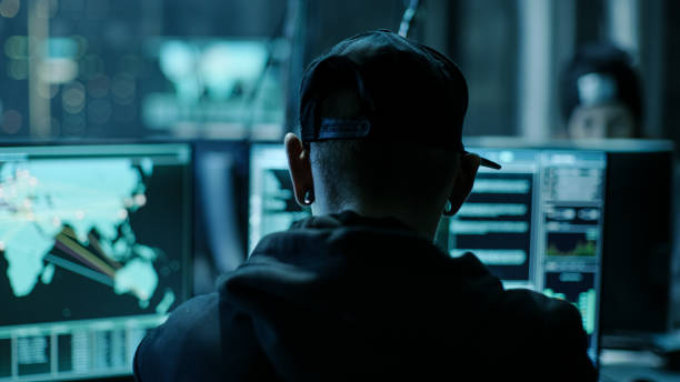 istock Close-up Frame from the Back of Working Hacker Organizing Advanced Virus Attack on Corporate Servers. Place is Dark and Has Multiple displays. 817486368