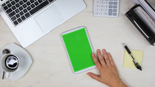 istock woman using a mobile phone /  tablet PC with green screen at her desk in the office - top view 817544902