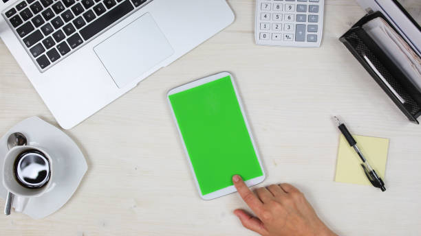 istock woman using a mobile phone /  tablet PC with green screen at her desk in the office - top view 817544966