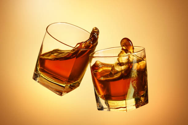 istock Two whiskey glasses clinking together on brown 817547834