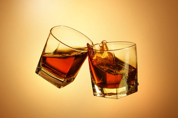 istock Two whiskey glasses clinking together on brown 817548620