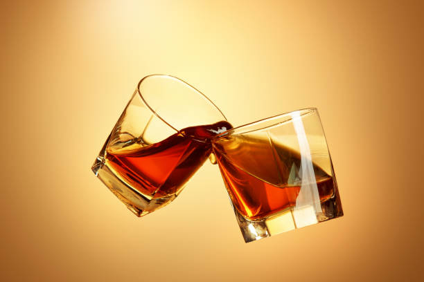 istock Two whiskey glasses clinking together on brown 817548724