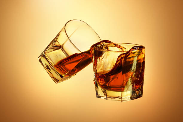 istock Two whiskey glasses clinking together on brown 817548924