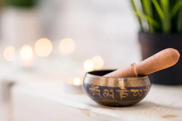 An indoor yoga studio is decorated with small plants and candles. Here a singing bowl used to lead meditation is in the front of the frame.